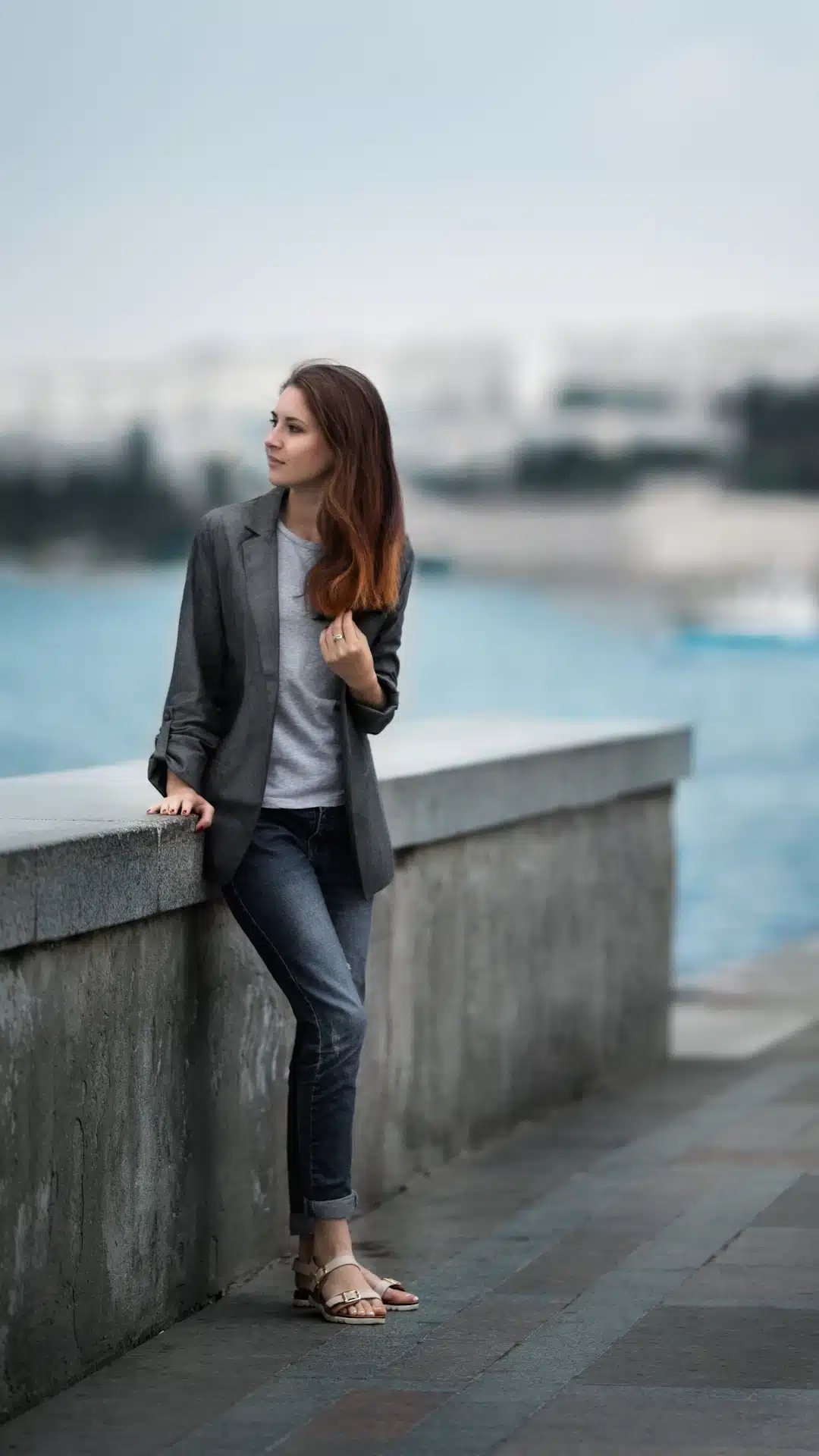 woman in gray blazer and blue denim jeans standing on gray concrete wall during daytime