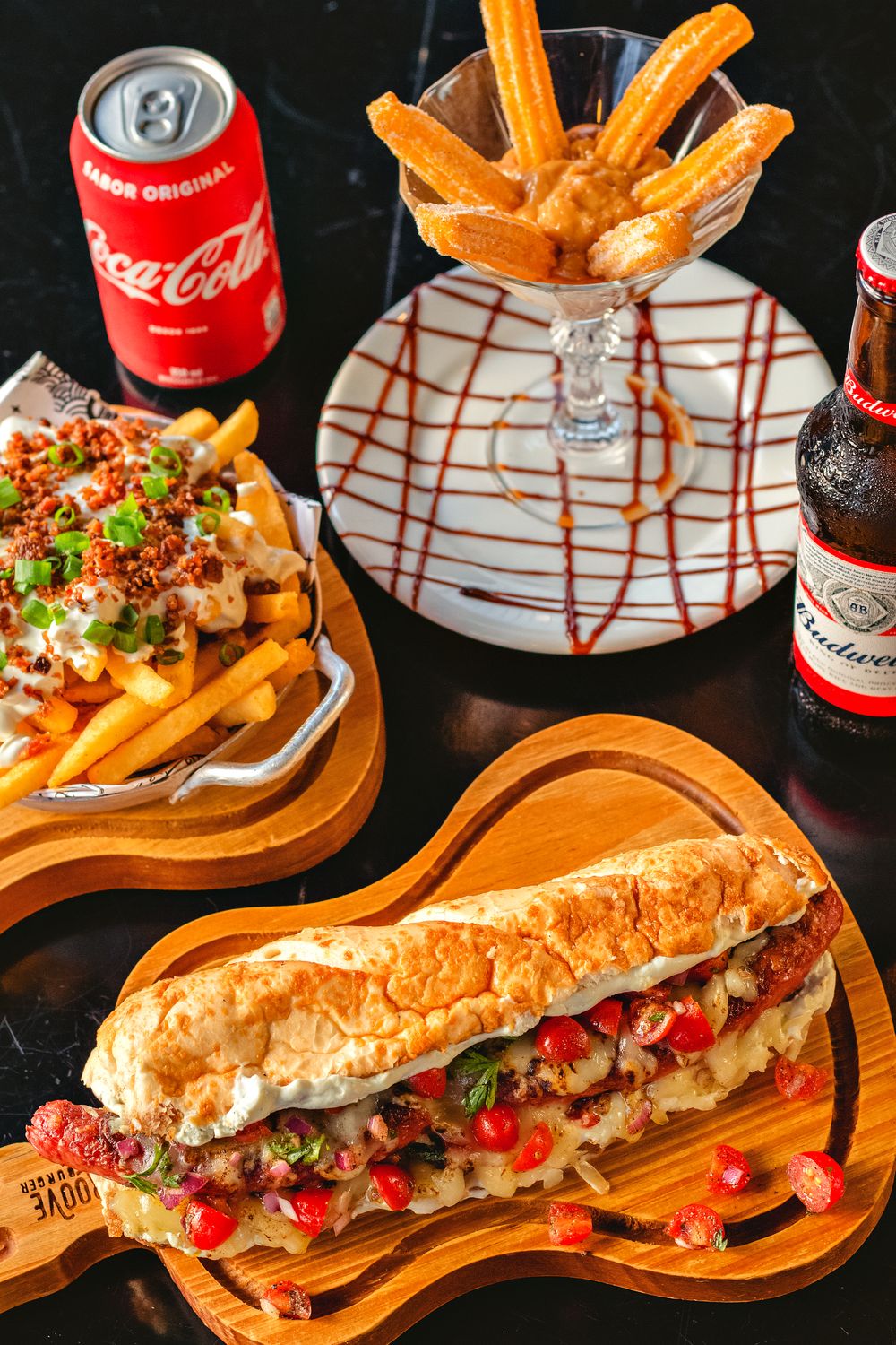 Appetizing sandwich with loaded fries, churros, and drinks on a table.