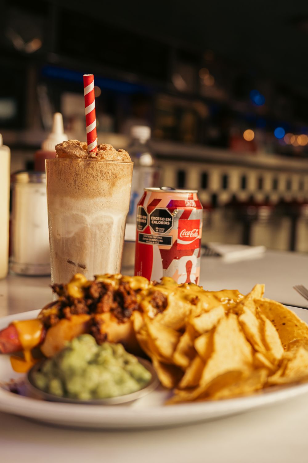 Delicious diner meal featuring loaded nachos, a creamy milkshake, and a soda can on a retro counter.