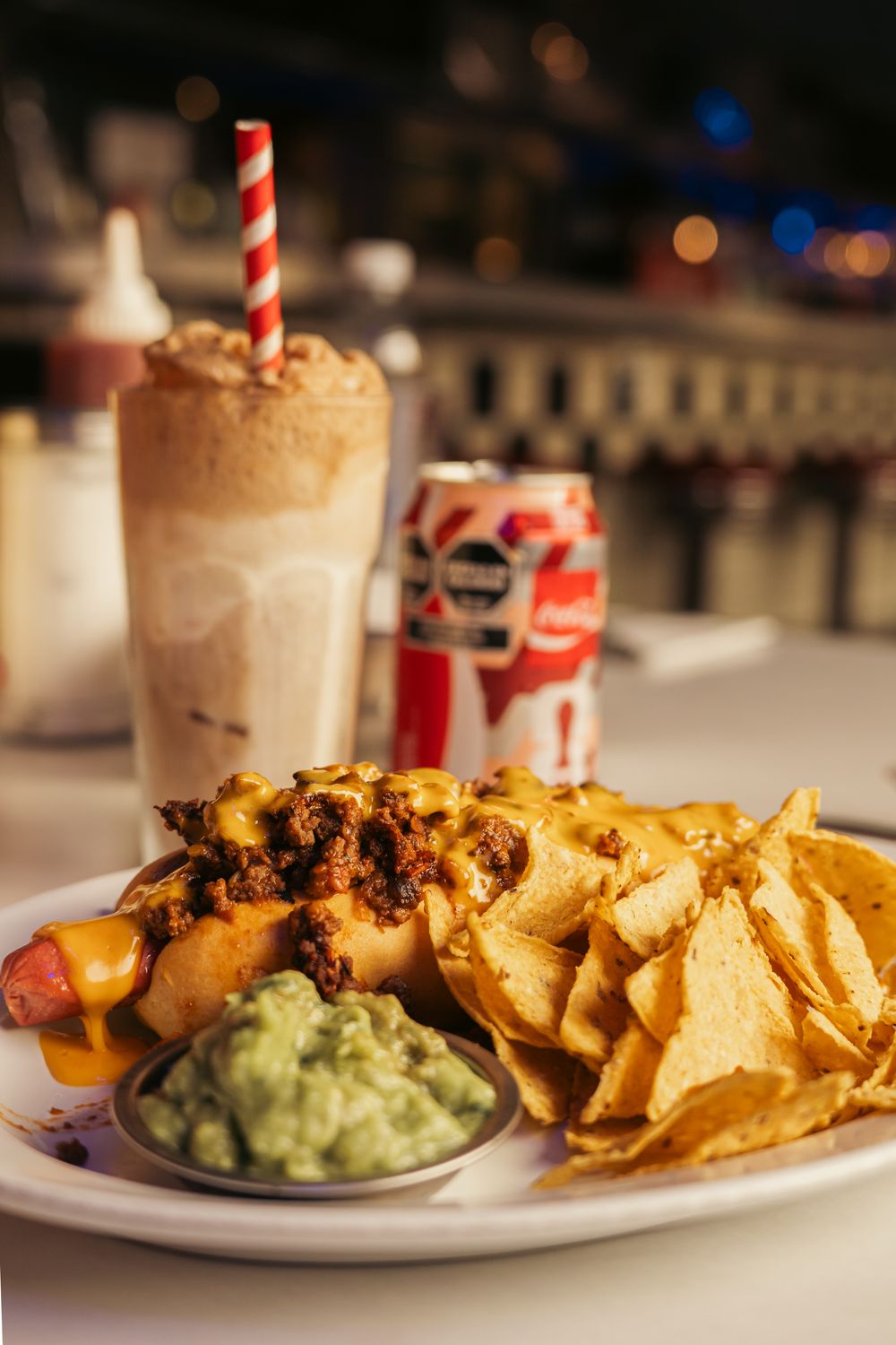 Savor a chili cheese hot dog with nachos, guacamole, soda, and milkshake in Buenos Aires diner setting.